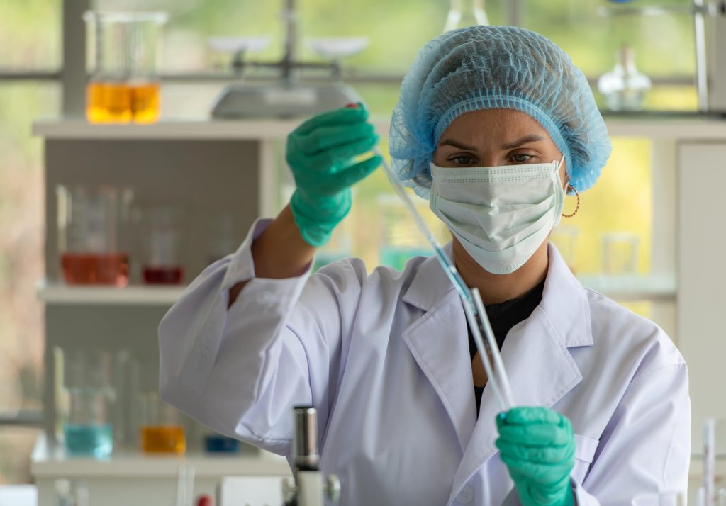 Technician in gown, mask and gloves pipetting in a pharmaceutical production laboratory